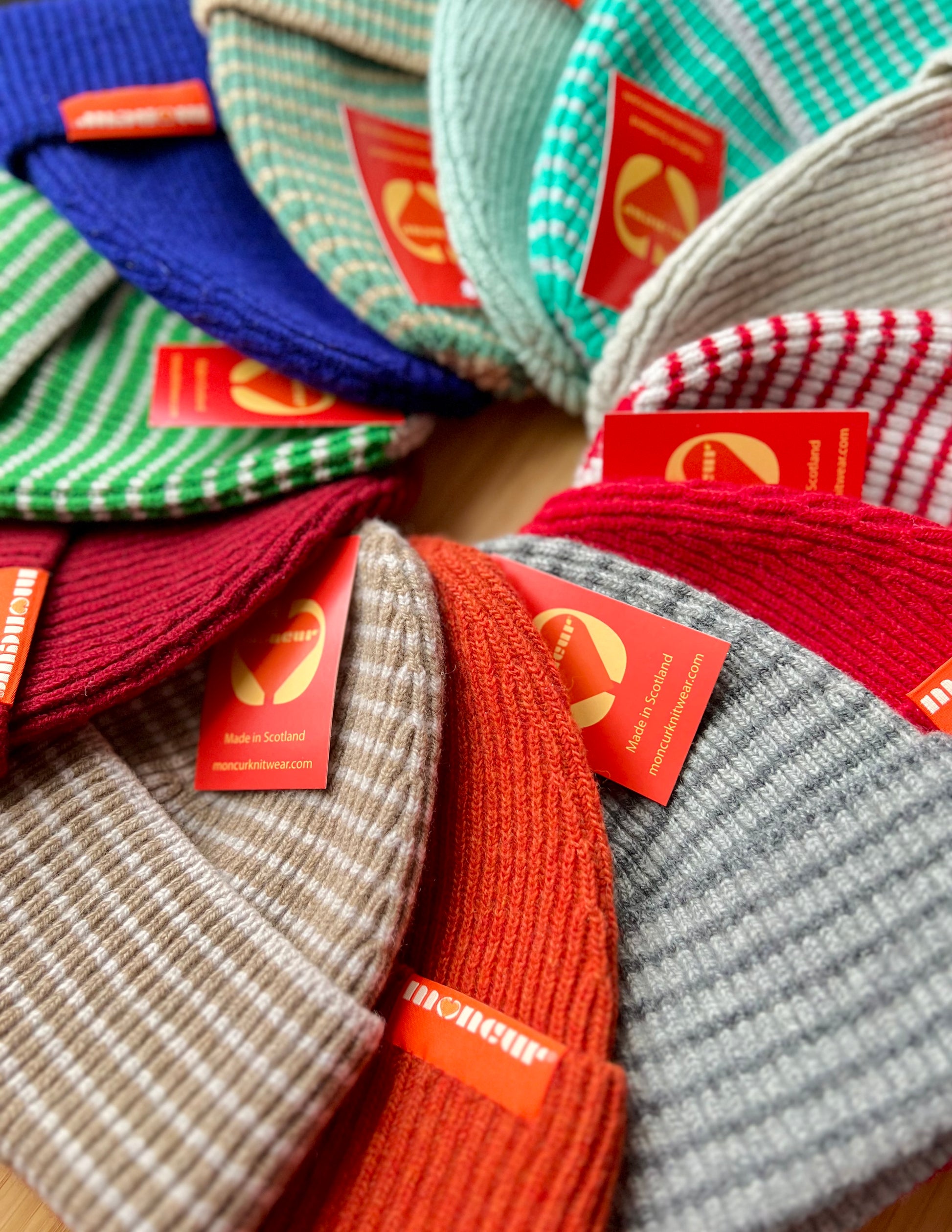 A collection of ribbed knit hats in various colors, including red, green, blue, and orange, with tags attached indicating brand.
