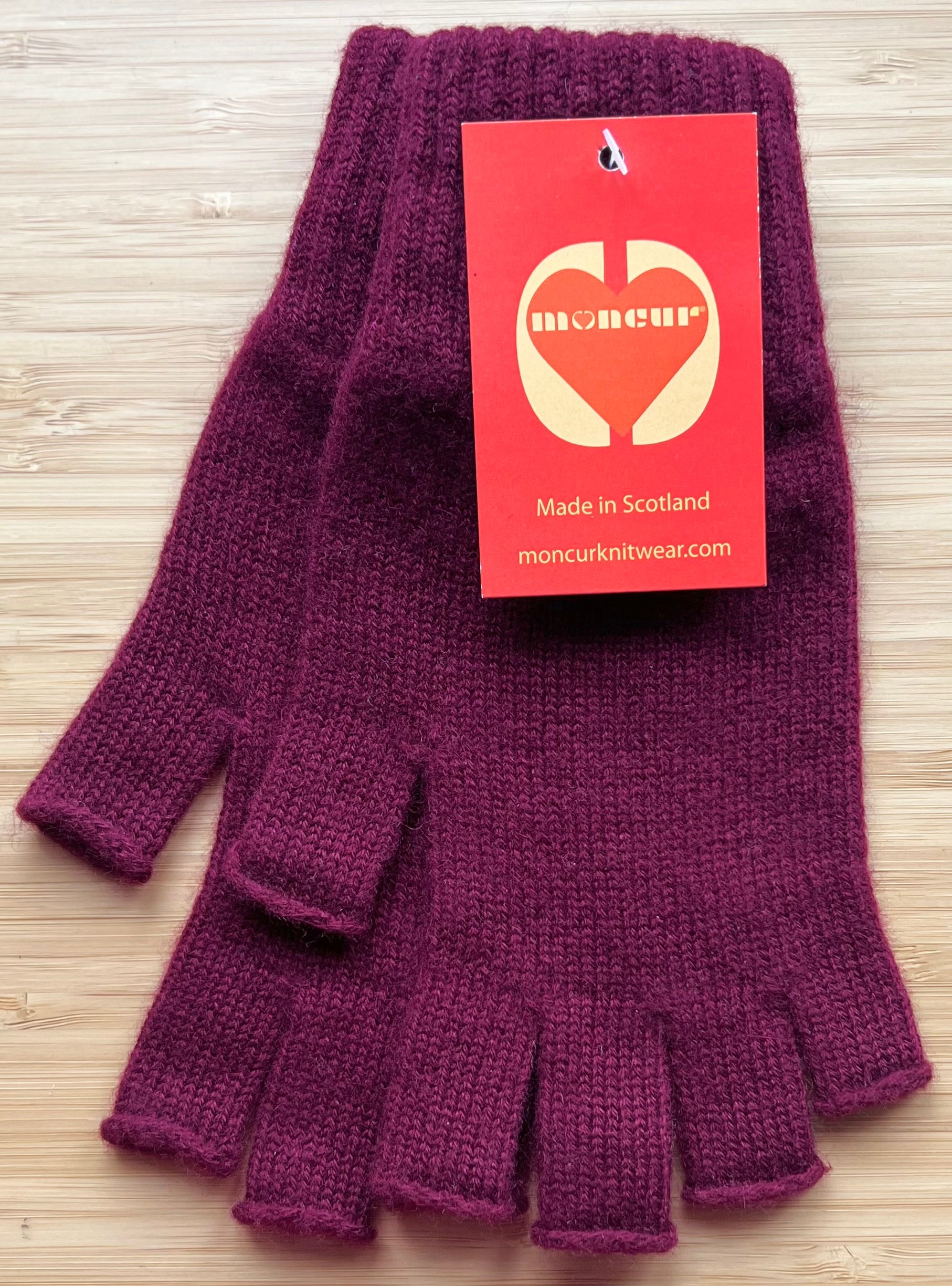 A pair of burgundy cashmere fingerless gloves  with tags indicating the brand Moncur Knitwear.